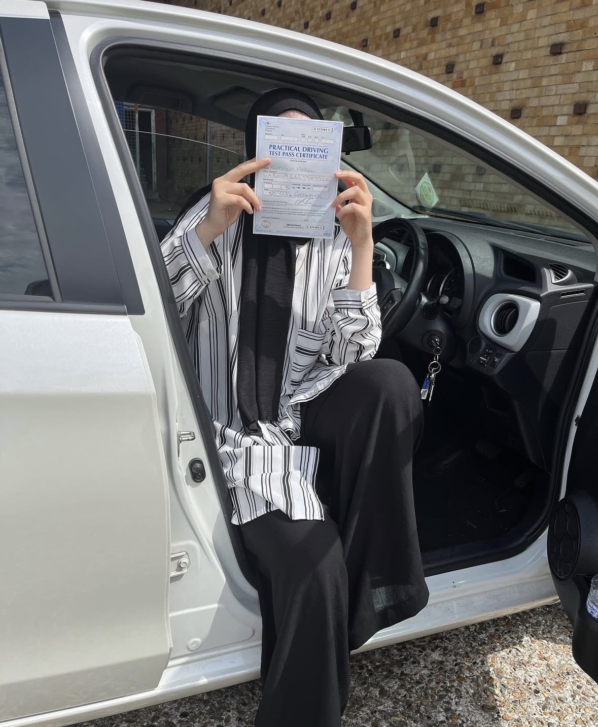 Learner holding their practical driving test pass certificate in the car